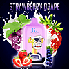 A RandM Digital Box 12000 vape device labeled "Fumot" with an illustrated character resembling an angry monkey wearing an eyepatch, set against a background of strawberries, grapes, and splashes of milk, with the flavor text "Strawberry Grape" above.