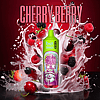A green "RandM Tornado" vape device with a colorful, cartoonish design is surrounded by splashes of milk and various berries, including raspberries, blackberries, and cherries, with the text "CHERRY BERRY" at the top.