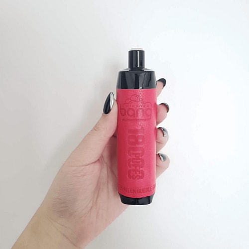 A hand holding a red vape device with black accents against a white background.